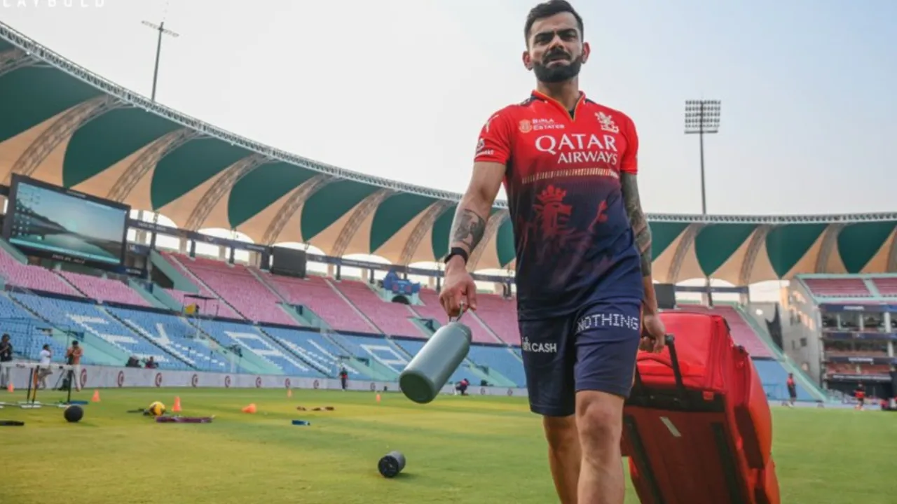Virat Kohli walking on the cricket ground during a team practice session, carrying sports gear and a water bottle at a stadium.