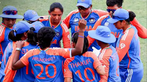 India Women cricket team huddle during ICC Women's T20 World Cup match — players including Harmapreet Kaur and Smriti Mandhana in blue and orange jersey