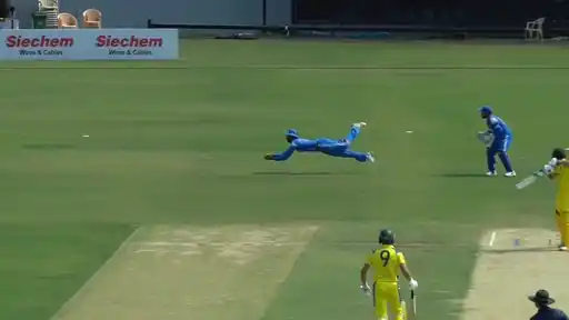 India A fielder in blue dives full length to take a stunning catch against Australia A at Puducherry, with the wicketkeeper watching and a batter in yellow at the crease