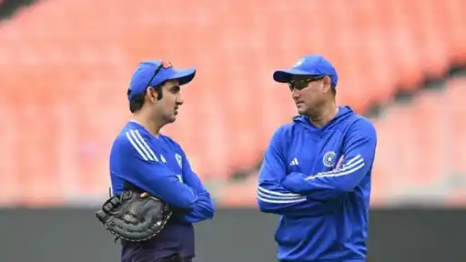 Two India staff members in blue training kit and caps talk with arms crossed in an empty stadium, as Gautam Gambhir pens an emotional message for Ajit Agarkar's exit as chief selector