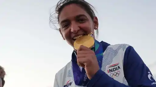 Harmanpreet Kaur smiling and biting her Asian Games 2026 gold medal in an India jersey, ahead of her emotional post on stepping down as India captain