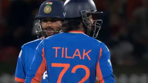 Two India batters in blue kit and navy helmets talk in the middle during the chase, one with his back to the camera in a jersey reading TILAK 72