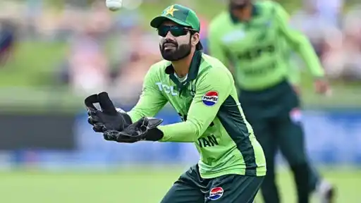 Rizwan in Pakistan’s green kit and sunglasses watches the ball into his gloves during a match, with a teammate blurred behind him