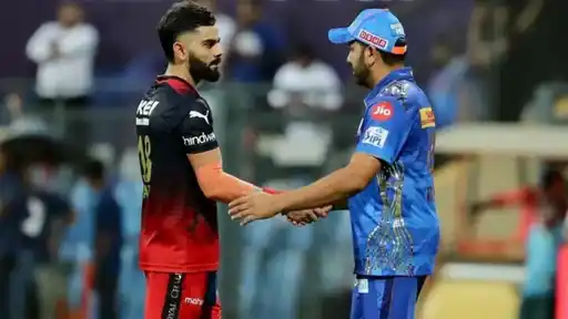 Two cricketers shake hands after an IPL match, one in a red and navy Royal Challengers Bengaluru jersey and the other in a blue Mumbai Indians jersey and cap.