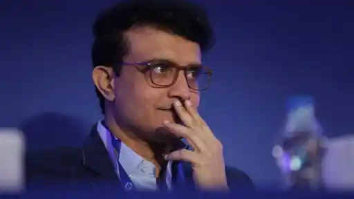 Sourav Ganguly, appointed Delhi Capitals head coach for IPL 2027, in glasses and a dark blazer with a hand on his chin against a blue background