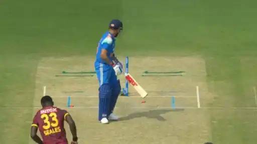 India batter in blue kit looks at his disturbed stumps after being bowled, with West Indies bowler Seales, shirt number 33, in the foreground during the IND vs WI 3rd ODI